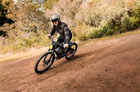 A helmeted rider leaning a Vintage into a dirt-road turn