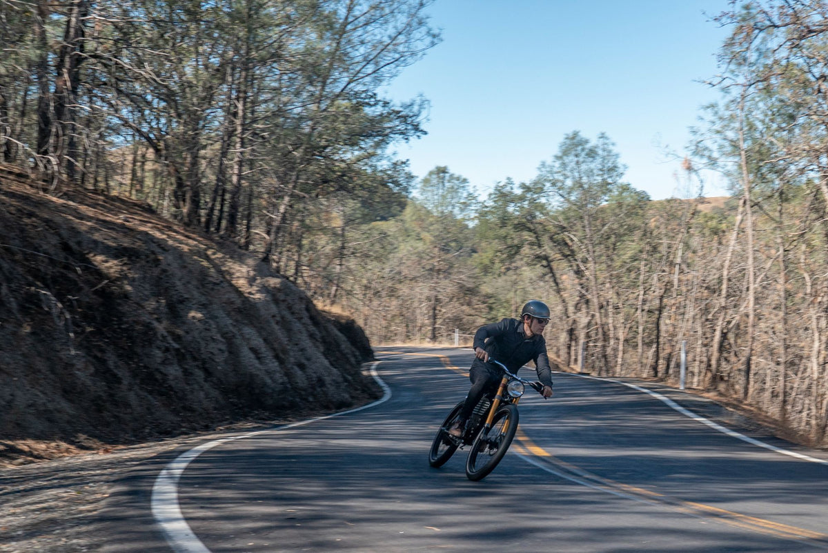 A helmeted Vintage rider carving through a winding road in the California woods