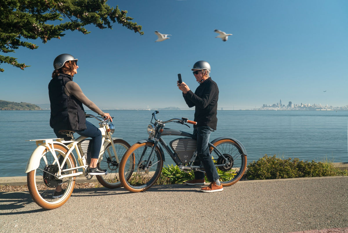 Two helmeted Vintage riders sharing a moment with their bikes beside San Francisco Bay